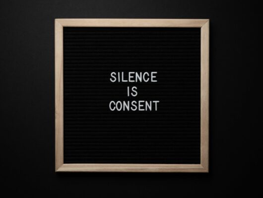 From above blackboard with written phrase SILENCE IS CONSENT on center on black background