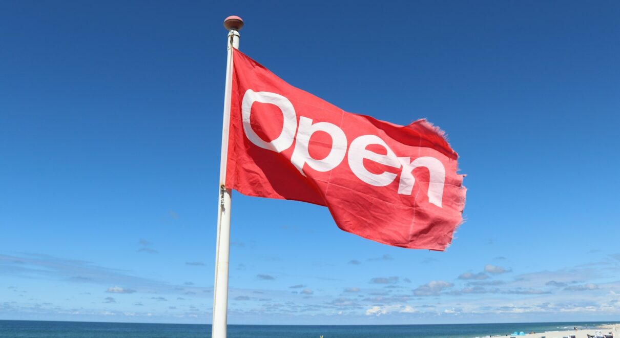 a red open flag on a beach next to the ocean